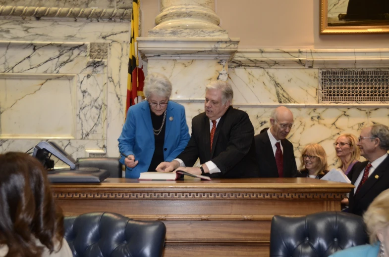 two men and one woman signing documents while sitting at a table