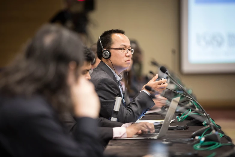 two men and woman sit on the sidelines of a conference room