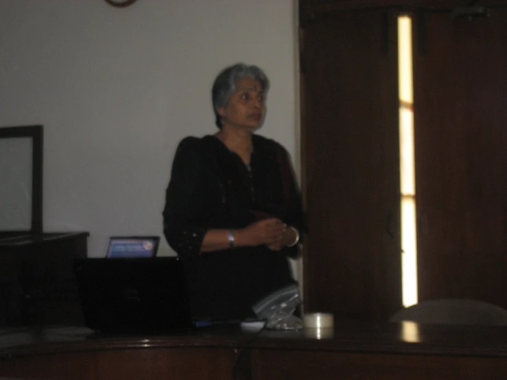 a woman standing with her arms folded next to a laptop computer