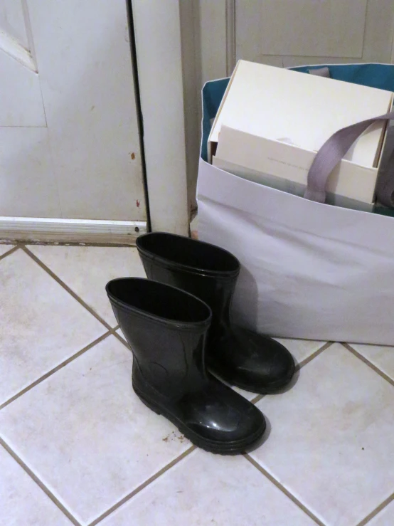 a pair of black rubber boots on the floor in front of a white bag