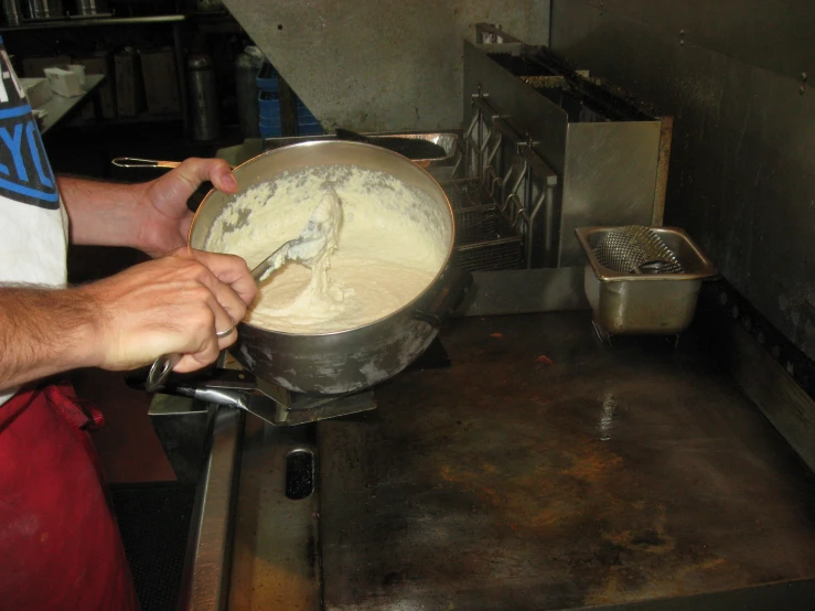 someone holding a metal bowl in front of an industrial type stove