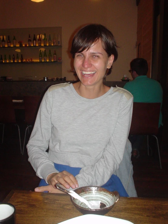 a smiling woman sits at a table and eats some food