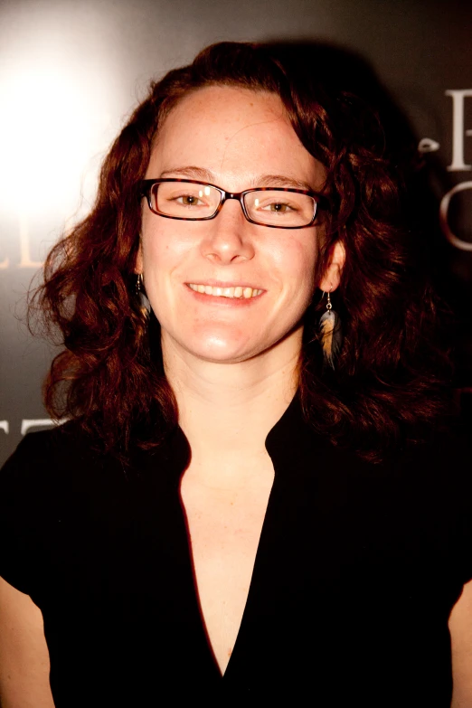 the smiling woman in glasses has dark brown hair and black dress