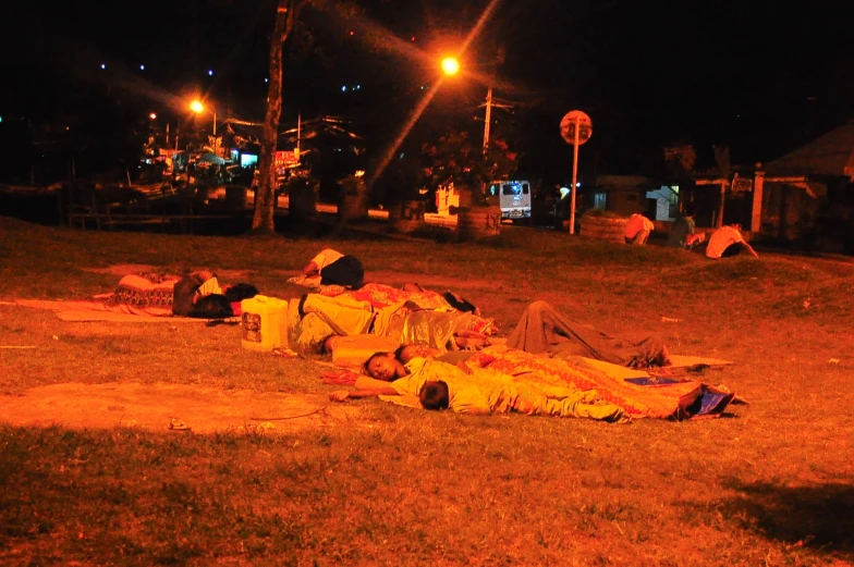 group of people sleeping on grass near street lights at night