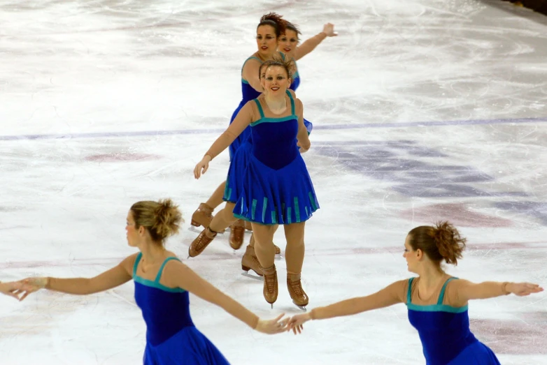 four ladies wearing blue figure dresses performing skate moves