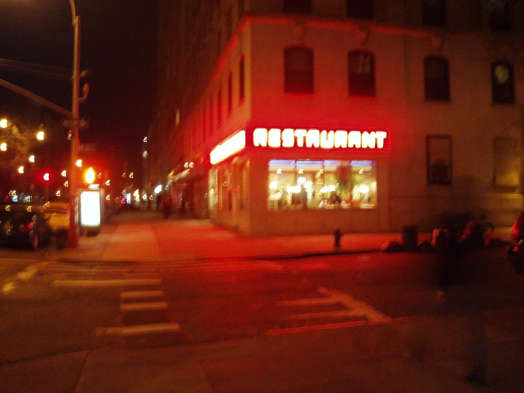 an empty crosswalk on a street with an illuminated restaurant at night