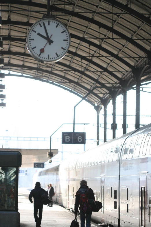 a clock hangs from the top of a train at a platform