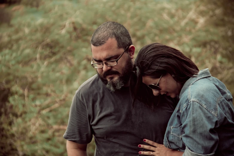 a man with glasses leaning on a woman as they both hug