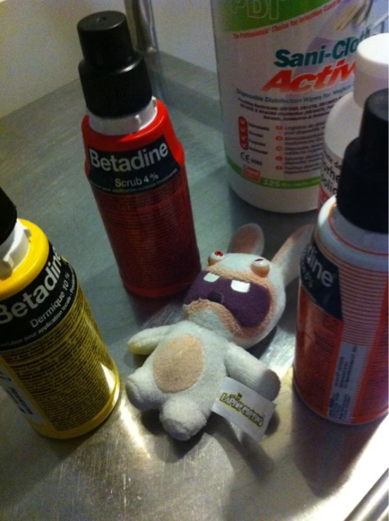 several spray bottles are on a metal sink next to a stuffed animal