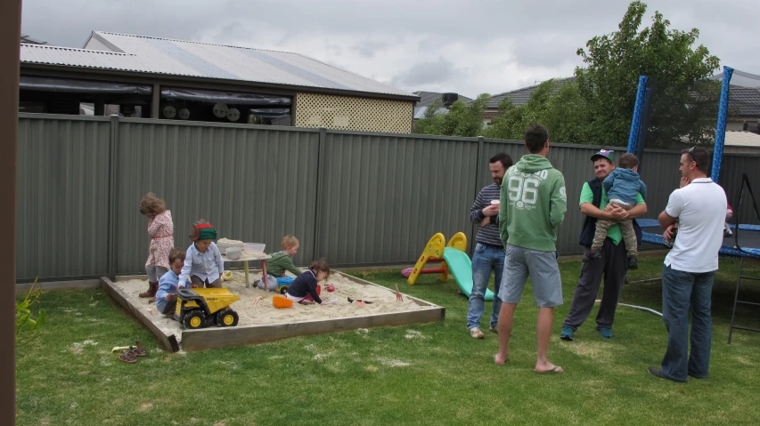 a family stands around a sand box playing in the yard