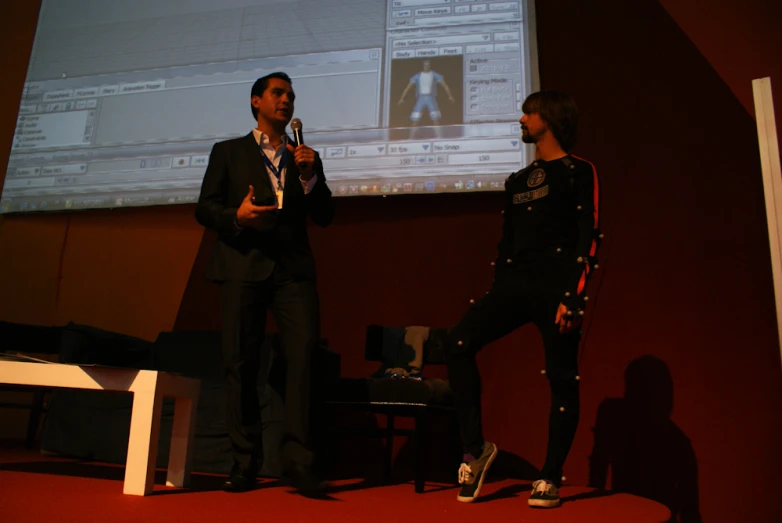 two people in suits are on stage with a projector screen