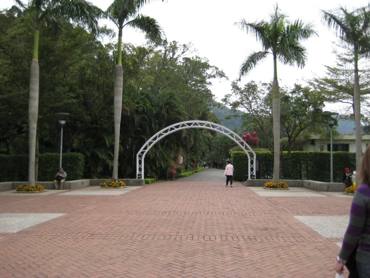 a person walking across a brick walkway and arch in a park
