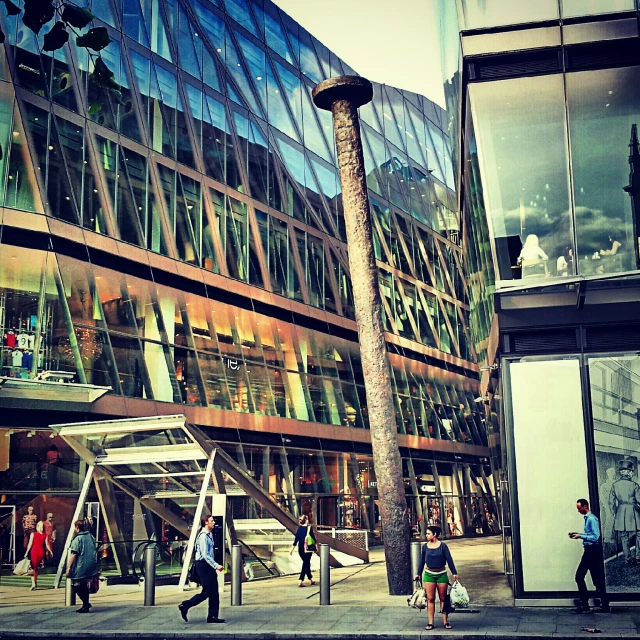 several people walking on the sidewalk in front of some glass buildings