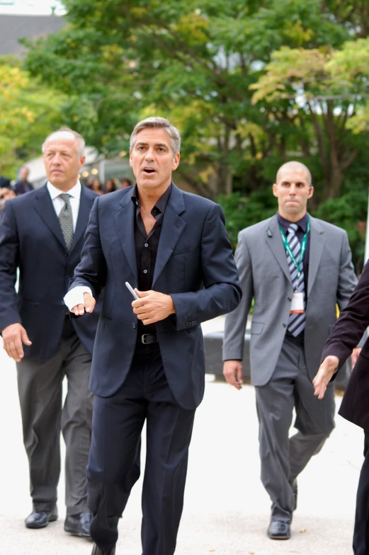 men in suits walk together in front of several trees