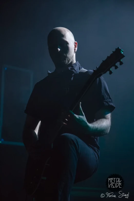 a man with bald head and a black shirt holding an electric guitar