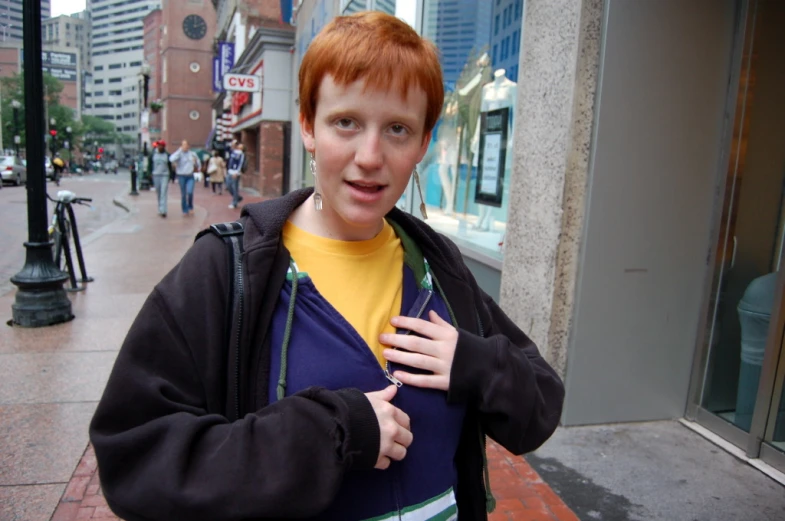a young red headed man in a sweatshirt is standing on the street