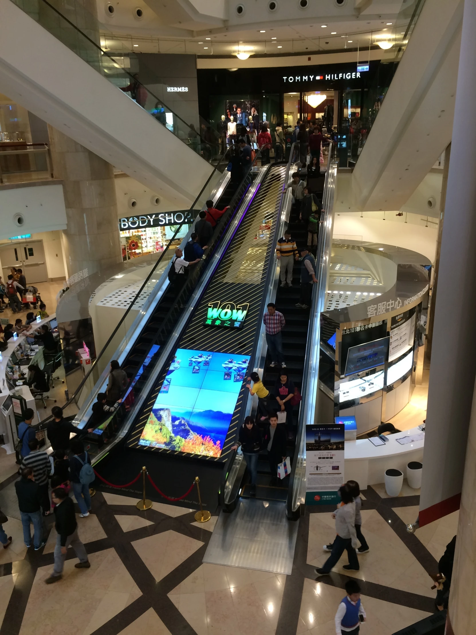 an escalator in a mall with people and a television