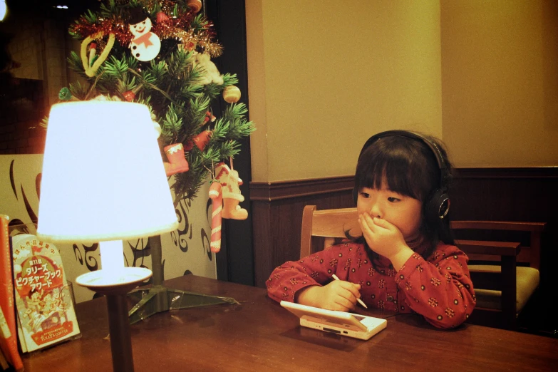 a girl sits at the table in front of a christmas tree