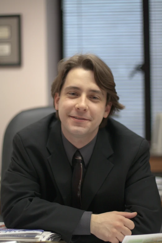 man in business suit seated at desk with arms crossed