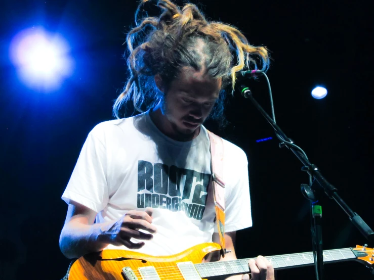 a male with long hair holding a yellow guitar in his hands