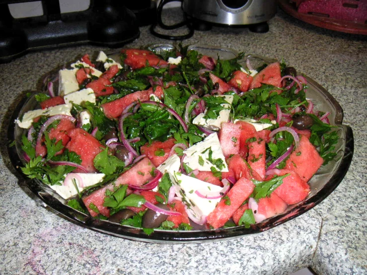 a bowl of salad that includes watermelon, onions and cheese