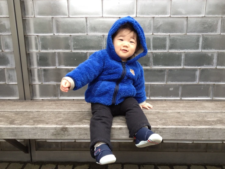 a little boy in a blue furry coat on a bench