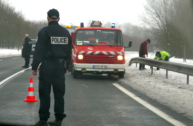 a man wearing a police uniform standing on a road next to police vehicles