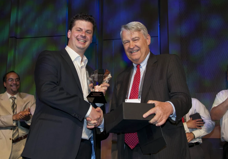 a couple of men standing next to each other holding up an award