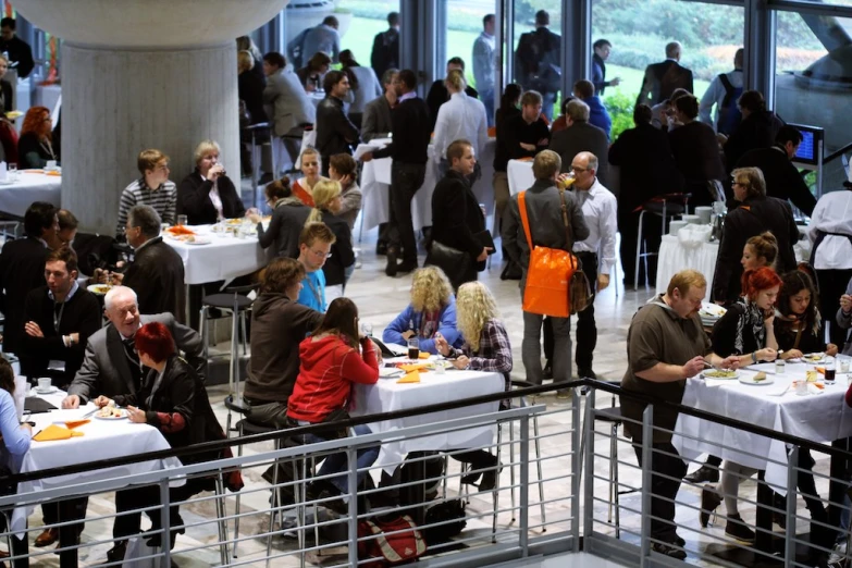 many people eating lunch in a building with big windows