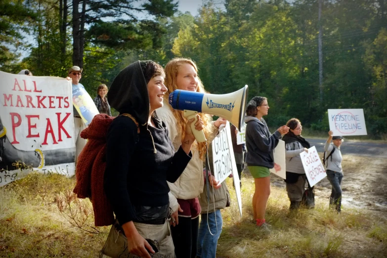 two women are on the phone outside and there is a woman in a crowd holding a sign that reads all market peak