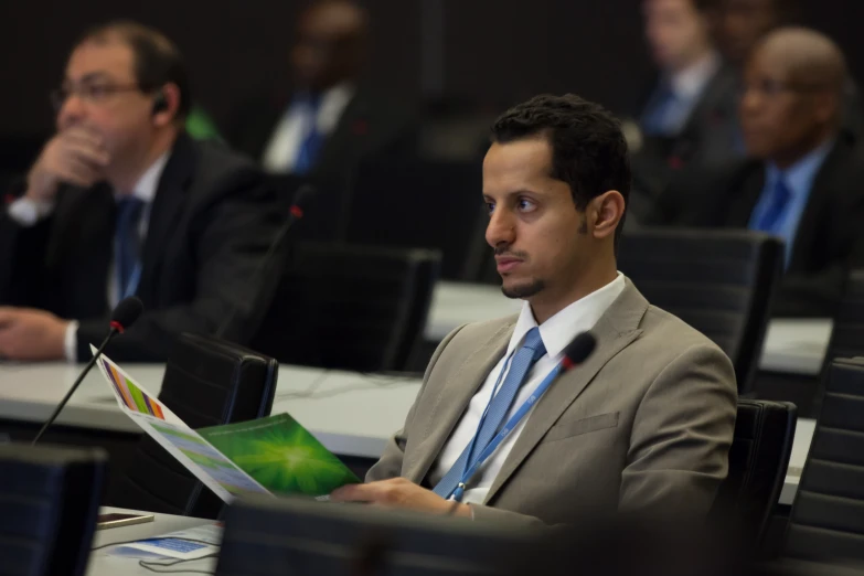 a man wearing a suit and tie looks at his laptop in front of other men