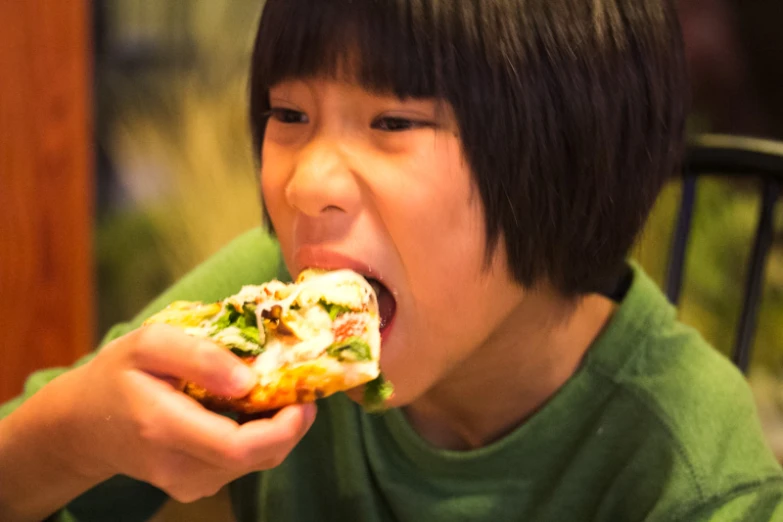 a  in a green shirt eating a slice of pizza