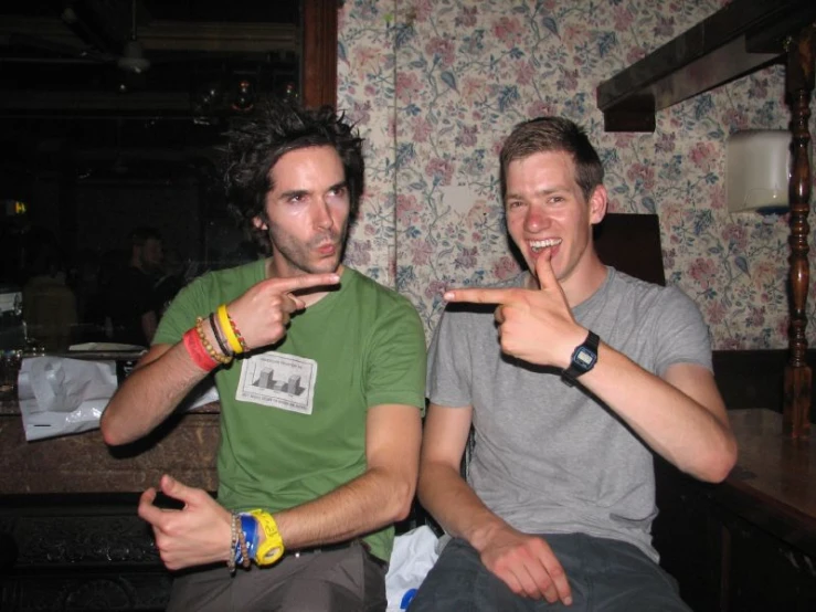 two men sitting on a counter point their finger in the camera