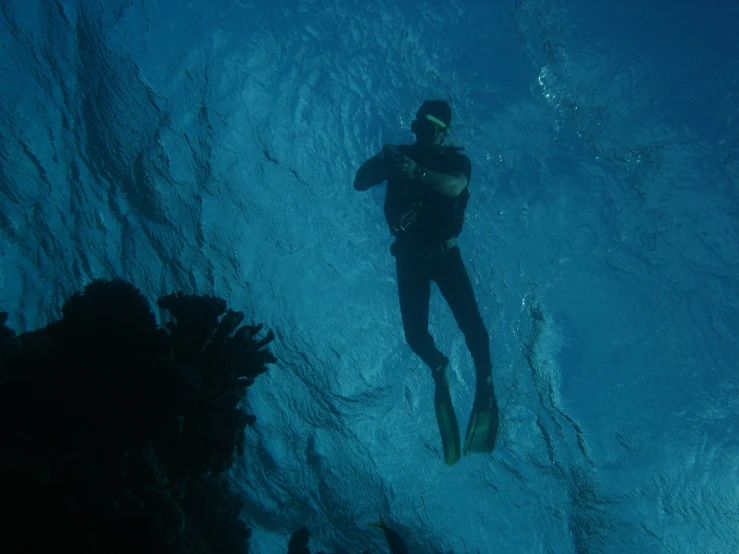 a scuba is seen in the blue water while he holds his hand up