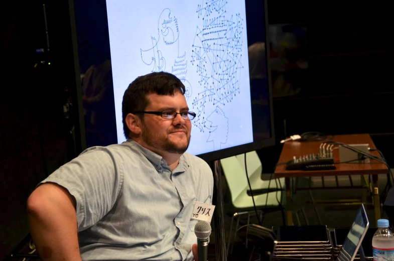 a man sitting at a desk with an animated screen in the background