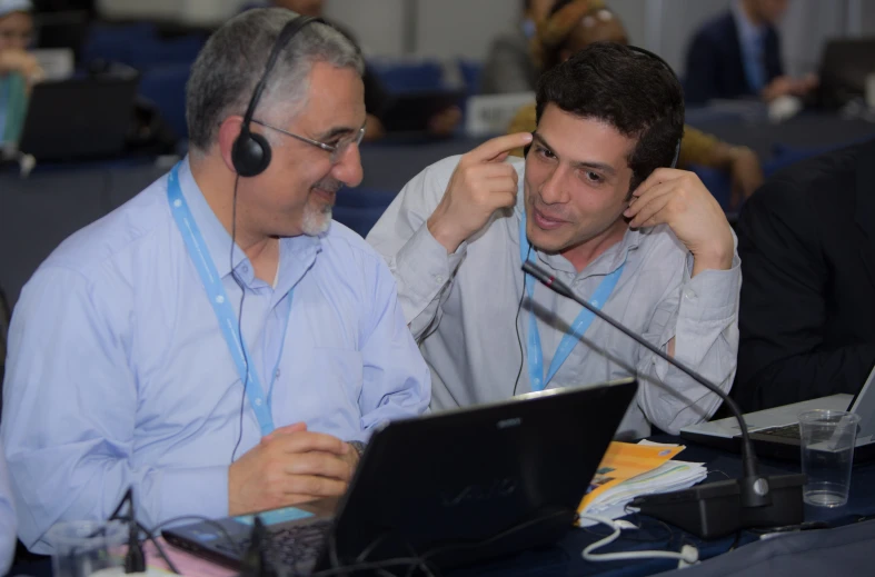 two men talking while using their laptop computers