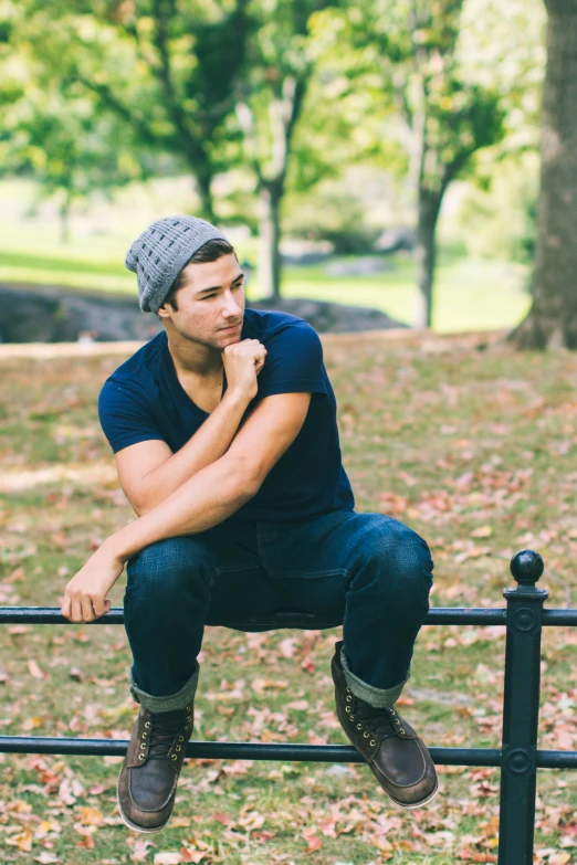 a man sitting on a black gate in front of trees