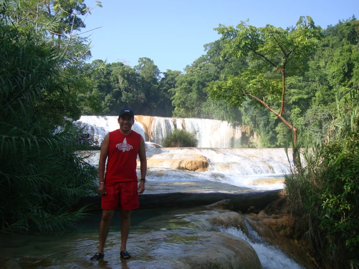 a man stands in the water and looks away from a waterfall