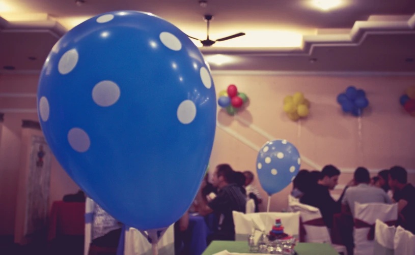 several people sitting at tables in the room where there is balloons