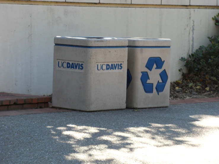 two trash cans on the pavement next to a building