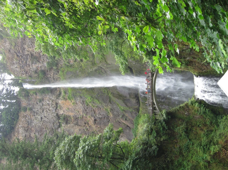 several people standing at the bottom of a waterfall with a small bridge across it