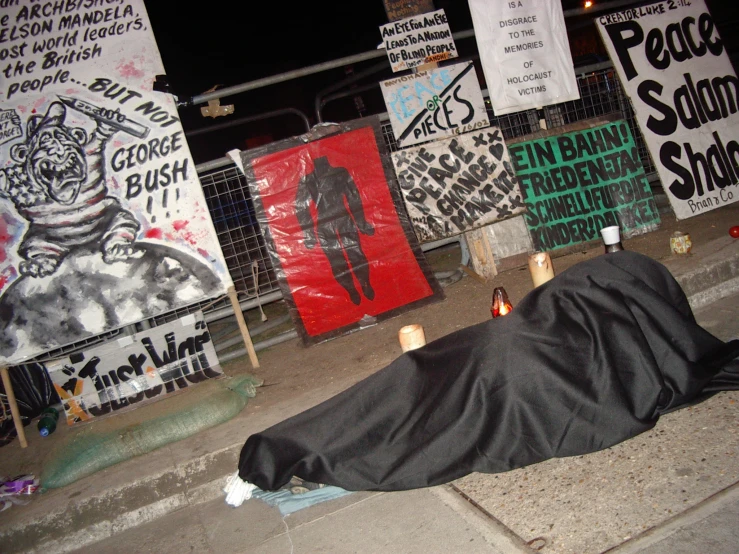 the homeless man lies on the sidewalk next to a wall of protest posters