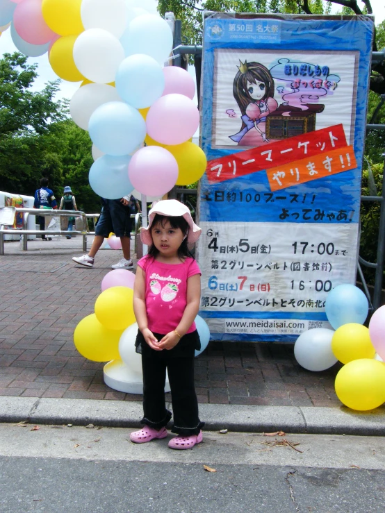 a little girl stands next to a large poster and balloon arch