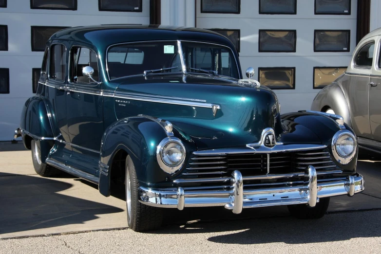 a green classic car sits parked beside another antique car