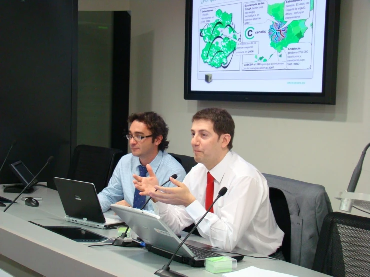 two men in business attire in front of a projector screen