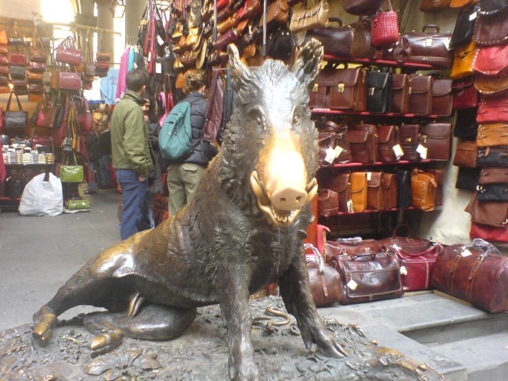 a bronze pig on display in a store with a lot of bags behind him