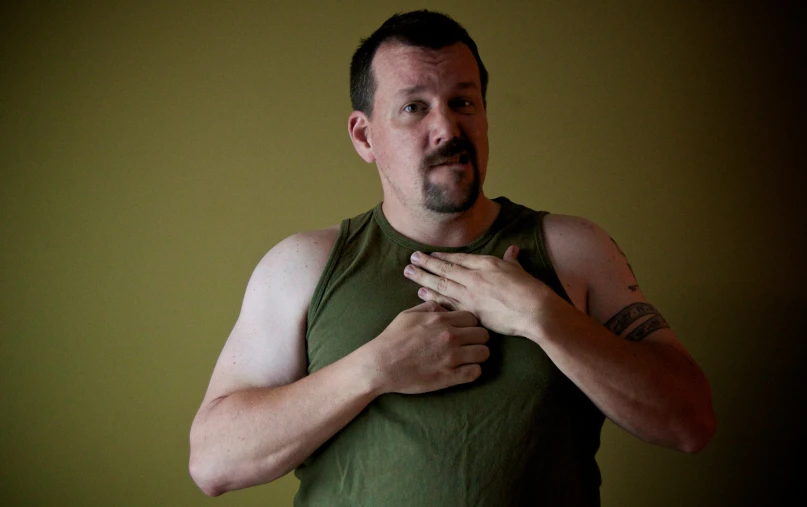 a man wearing a tank top and standing in front of a green wall