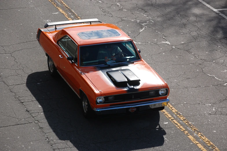 an orange muscle car sits in the middle of the street