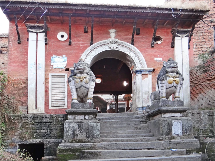 two statues at the top of the steps outside of an old brick building