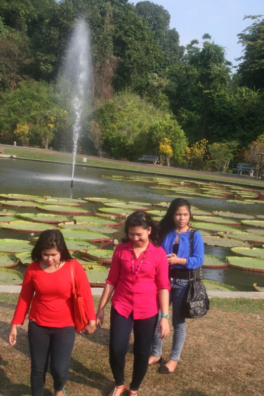 three women walking down a street next to an ornamental water fountain